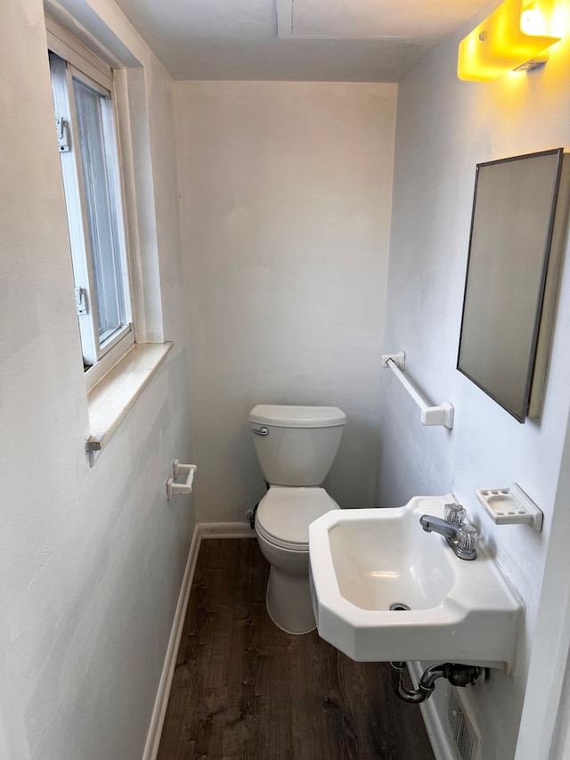 half bath with wood finished floors, toilet, baseboards, and a sink