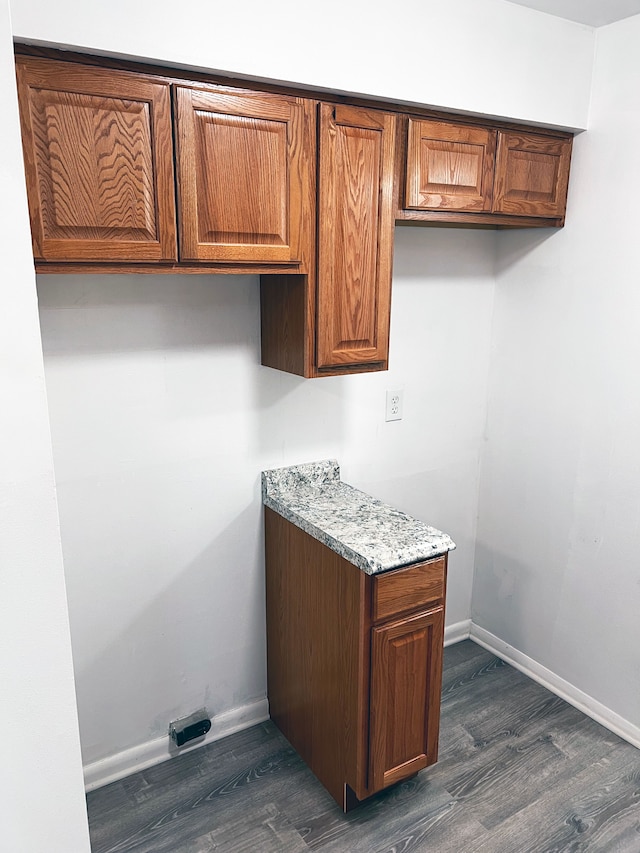 kitchen with dark wood-type flooring, light stone counters, baseboards, and brown cabinets