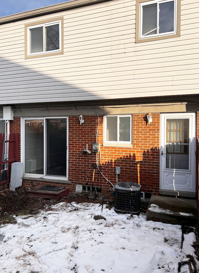 snow covered house featuring brick siding, central AC, and entry steps