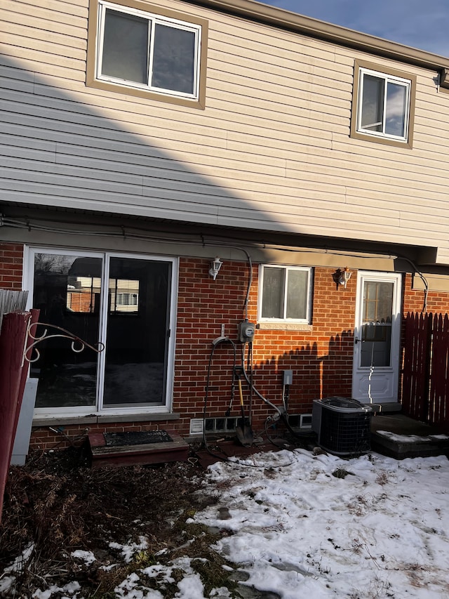 snow covered house with fence, central AC unit, and brick siding