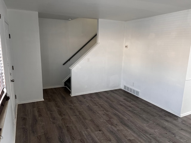 empty room featuring stairway, baseboards, visible vents, and dark wood-style flooring