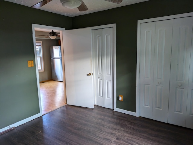 unfurnished bedroom featuring stainless steel refrigerator, ceiling fan, dark hardwood / wood-style flooring, a textured ceiling, and two closets