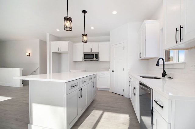 kitchen with hanging light fixtures, sink, appliances with stainless steel finishes, a kitchen island, and white cabinetry