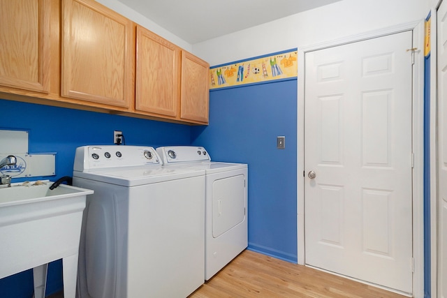 clothes washing area with washer and dryer, cabinets, light wood-type flooring, and sink