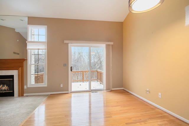 unfurnished living room featuring a towering ceiling, a fireplace, and light wood-type flooring