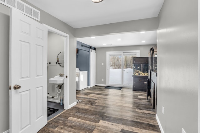 corridor with a barn door, dark wood-type flooring, and washer / clothes dryer