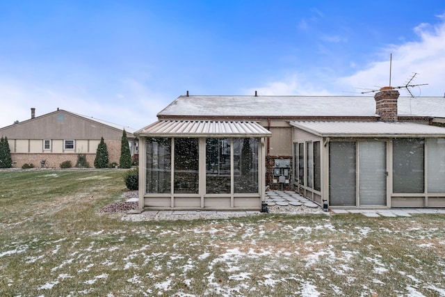 snow covered back of property with a yard and a sunroom