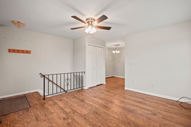 spare room with baseboard heating, light wood-type flooring, and ceiling fan with notable chandelier