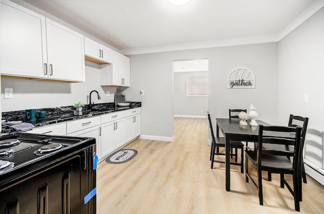 kitchen featuring crown molding, sink, dark stone countertops, white cabinets, and light hardwood / wood-style floors