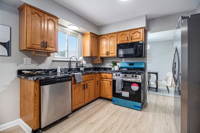 kitchen with dark stone counters, sink, stainless steel appliances, and light wood-type flooring