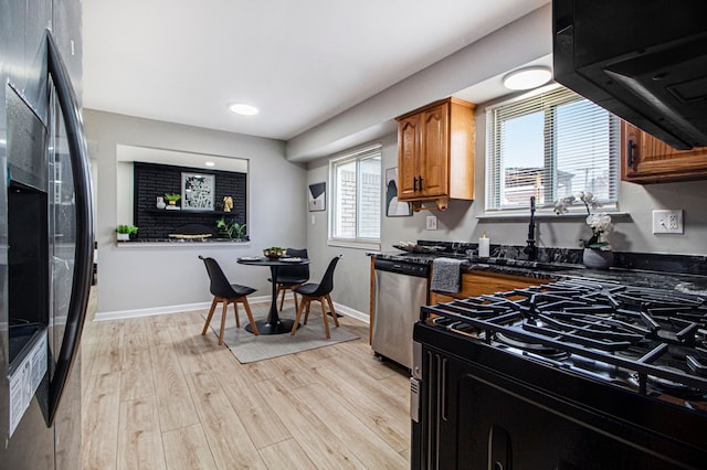 kitchen featuring black appliances, dark stone countertops, light wood-type flooring, and sink