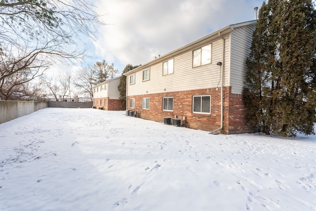 snow covered rear of property featuring central AC unit