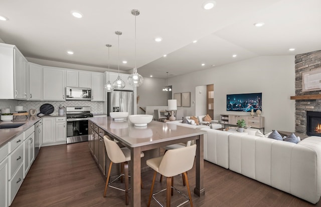 kitchen featuring appliances with stainless steel finishes, a fireplace, white cabinets, a center island, and lofted ceiling