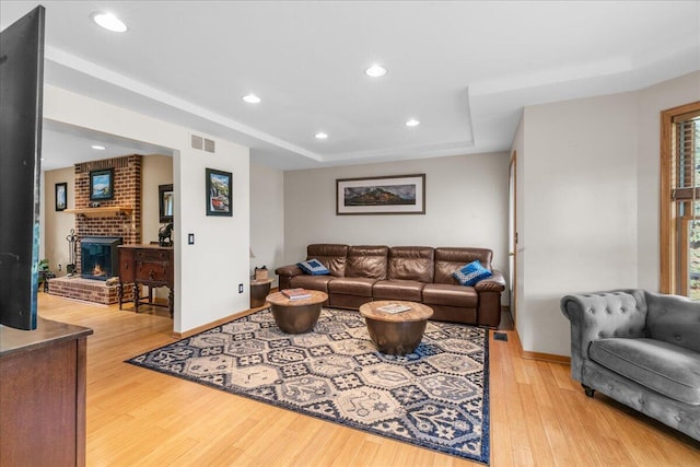 living room featuring light hardwood / wood-style floors, a raised ceiling, and a fireplace