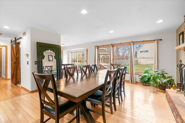 dining space with light wood-type flooring, plenty of natural light, and a barn door