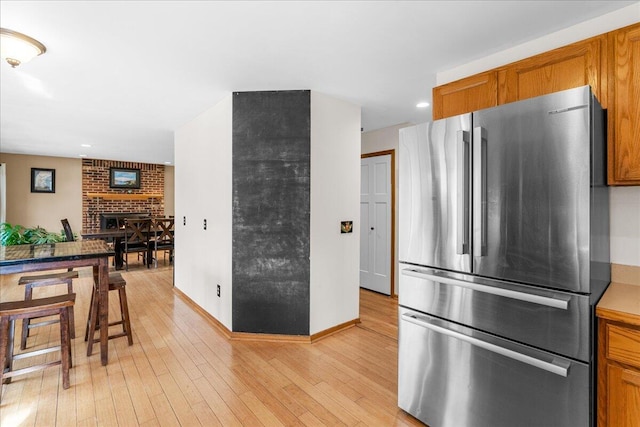 kitchen featuring stainless steel refrigerator, a fireplace, and light wood-type flooring