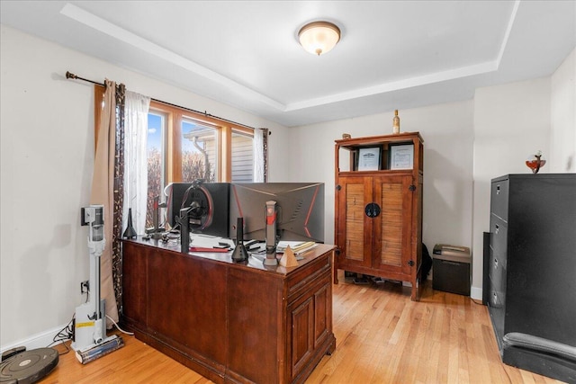 home office with light hardwood / wood-style floors and a tray ceiling