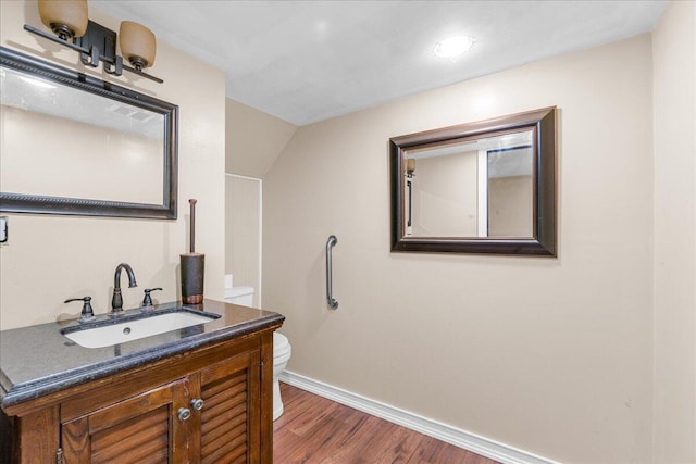 bathroom featuring toilet, vanity, hardwood / wood-style floors, and vaulted ceiling