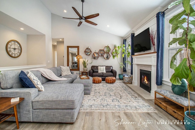 living room with ceiling fan, light hardwood / wood-style floors, lofted ceiling, and a brick fireplace