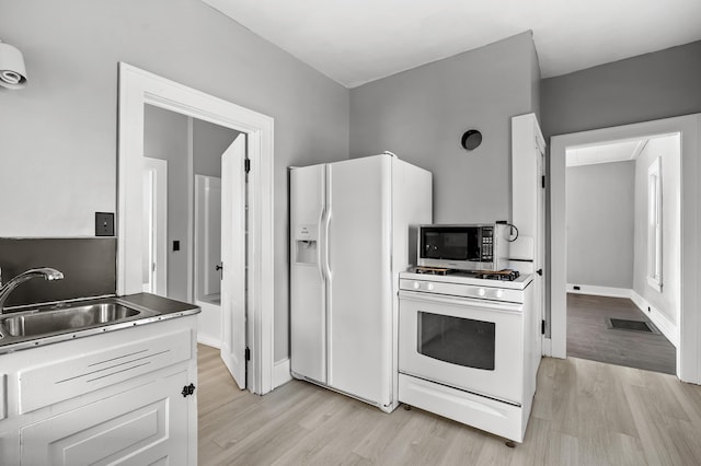 kitchen with white cabinetry, sink, white appliances, and light hardwood / wood-style flooring