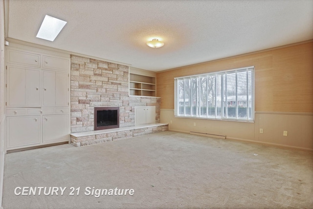 unfurnished living room with a skylight, a baseboard radiator, a stone fireplace, built in features, and a textured ceiling