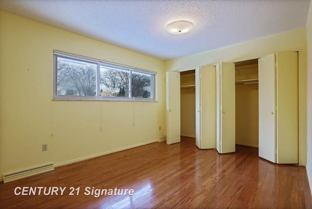 unfurnished bedroom featuring hardwood / wood-style floors, a textured ceiling, baseboard heating, and multiple closets