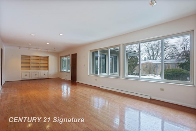 unfurnished living room featuring light wood-type flooring, a baseboard radiator, and a wealth of natural light