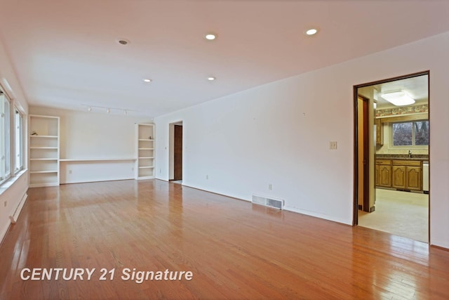 unfurnished room with built in shelves, light hardwood / wood-style floors, and sink