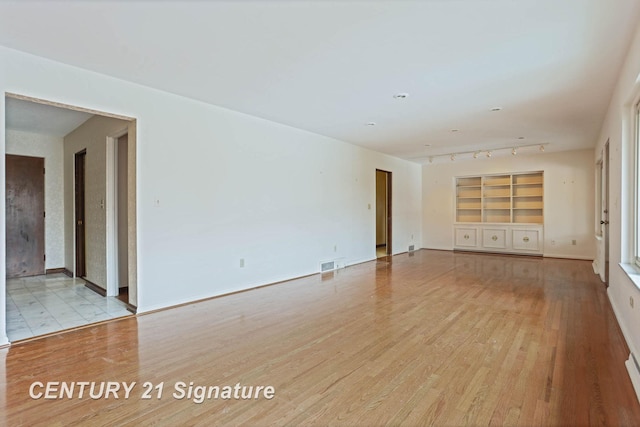 unfurnished room with built in shelves and light wood-type flooring