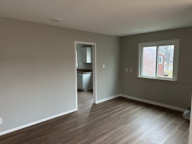 empty room with dark wood-type flooring and baseboards