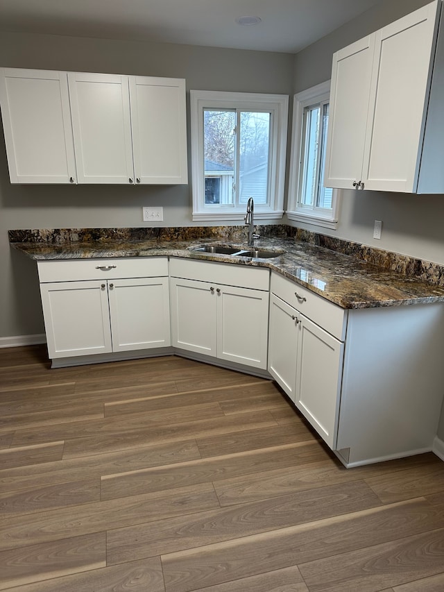 kitchen with dark stone countertops, white cabinetry, dark wood finished floors, and a sink