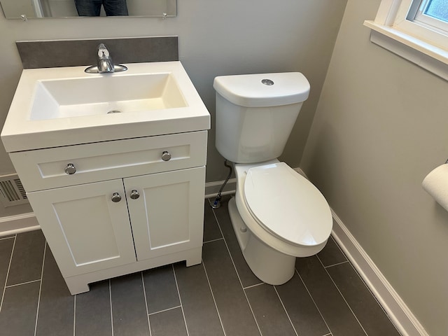 half bath with baseboards, visible vents, vanity, and toilet