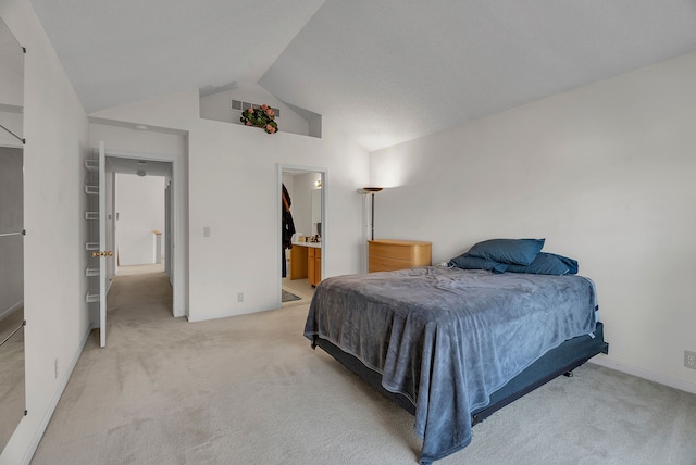 bedroom featuring ensuite bathroom, light colored carpet, and lofted ceiling