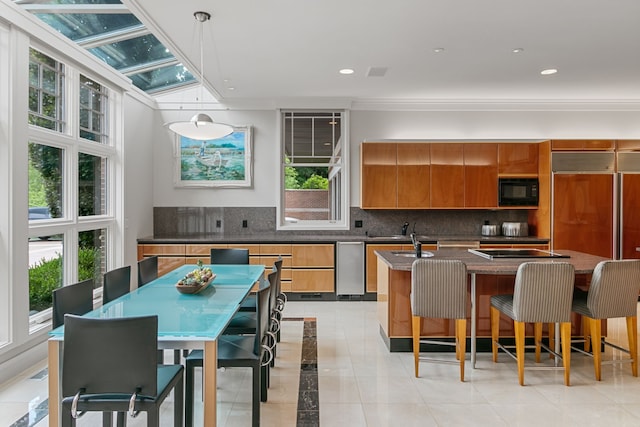 kitchen featuring tasteful backsplash, a breakfast bar, black microwave, pendant lighting, and an island with sink