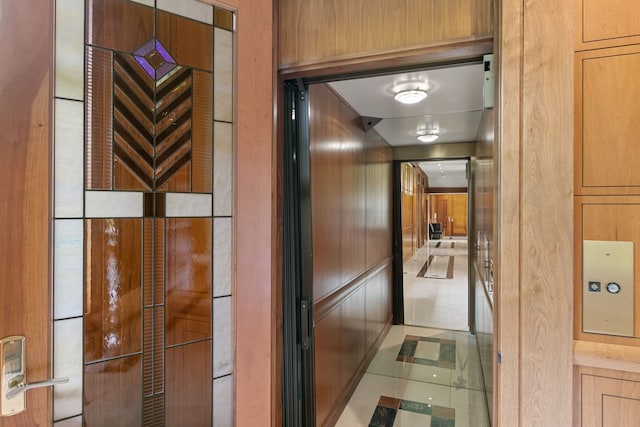 hallway featuring wooden walls, light tile patterned floors, and elevator