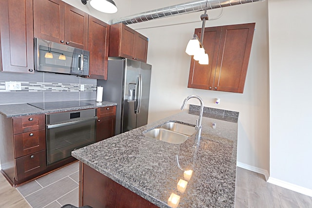 kitchen with decorative backsplash, appliances with stainless steel finishes, sink, dark stone countertops, and hanging light fixtures