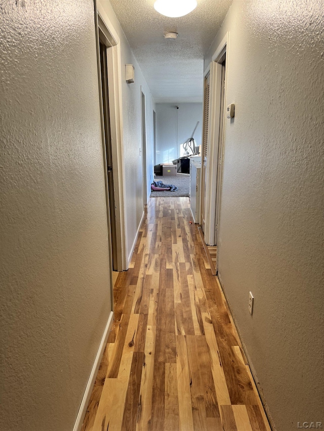 corridor with a textured ceiling and hardwood / wood-style flooring