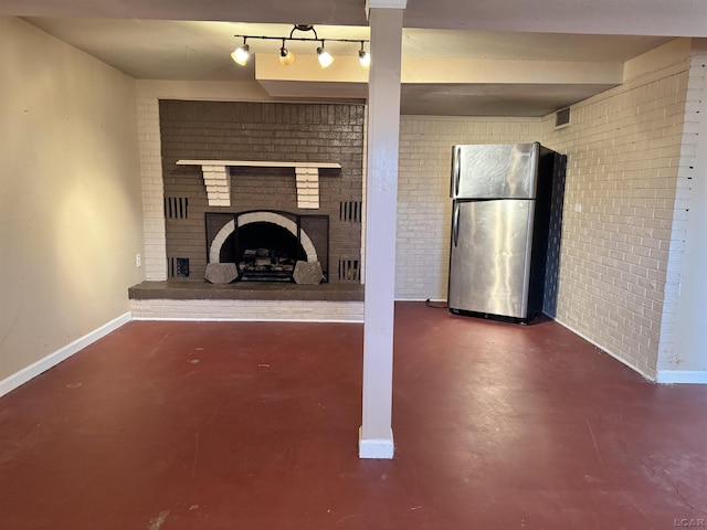 unfurnished living room with a fireplace, track lighting, and brick wall