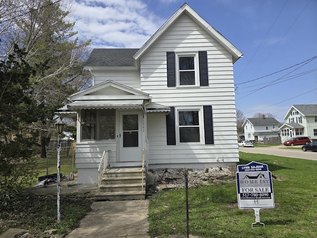 traditional-style home with entry steps, roof with shingles, and a front yard