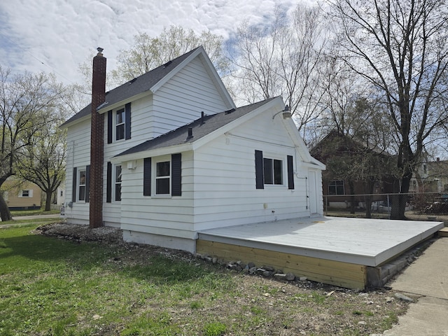 view of home's exterior featuring roof with shingles, a chimney, fence, a lawn, and a deck