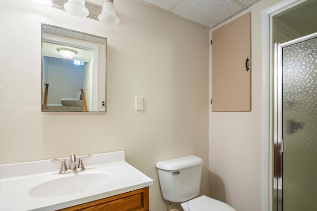 bathroom featuring vanity, a shower with door, toilet, and a drop ceiling