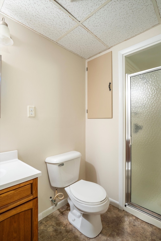 bathroom with a shower with door, vanity, a drop ceiling, and toilet