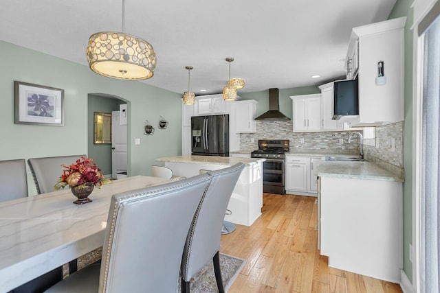 kitchen featuring white cabinetry, stainless steel appliances, wall chimney range hood, tasteful backsplash, and pendant lighting