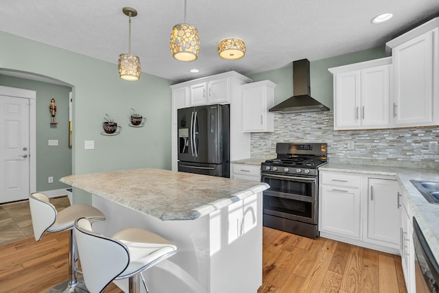 kitchen with backsplash, white cabinets, wall chimney range hood, hanging light fixtures, and stainless steel appliances