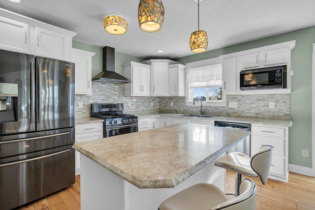 kitchen with a center island, sink, stainless steel appliances, wall chimney range hood, and pendant lighting