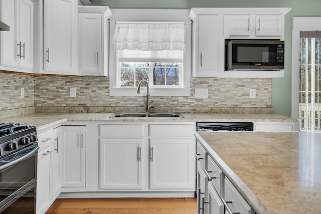 kitchen featuring white cabinets, sink, light wood-type flooring, tasteful backsplash, and stainless steel range with gas stovetop