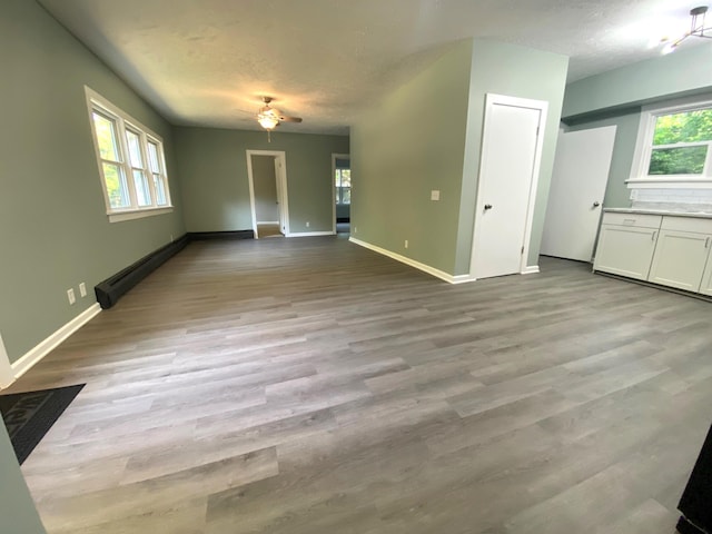 unfurnished living room featuring ceiling fan, a healthy amount of sunlight, light hardwood / wood-style floors, and a textured ceiling