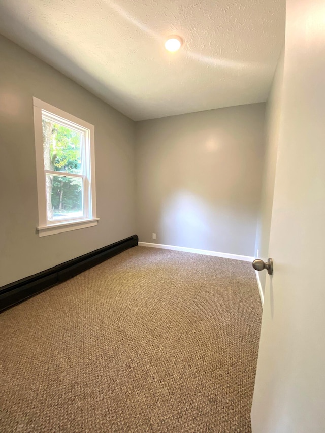 carpeted spare room with a textured ceiling and a baseboard heating unit