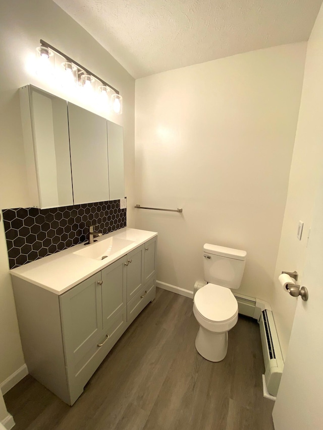 bathroom featuring vanity, a textured ceiling, a baseboard heating unit, hardwood / wood-style flooring, and toilet