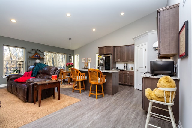 interior space featuring dark brown cabinetry, a center island, stainless steel refrigerator with ice dispenser, light hardwood / wood-style floors, and a breakfast bar